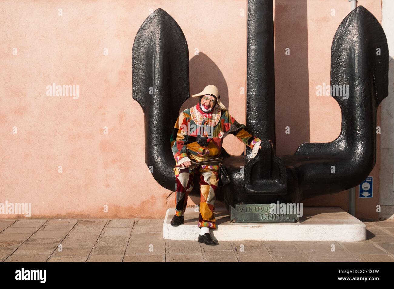 VENEZIA, ITALIA - 28 FEBBRAIO 2019: Maschera Harlequin seduta su una scultura a forma di ancora Foto Stock