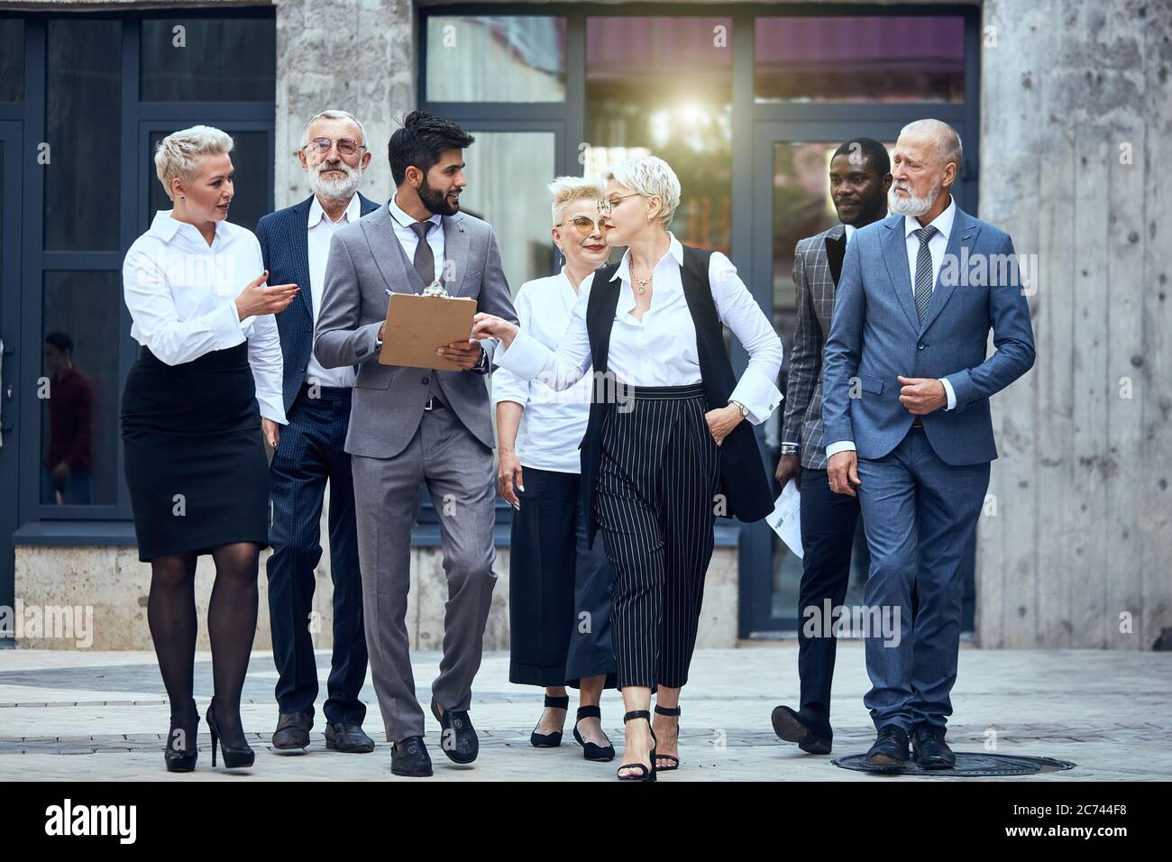 Gruppo di uomini d'affari vestiti in abiti eleganti da ufficio discutere progetto e muoversi in strada Foto Stock