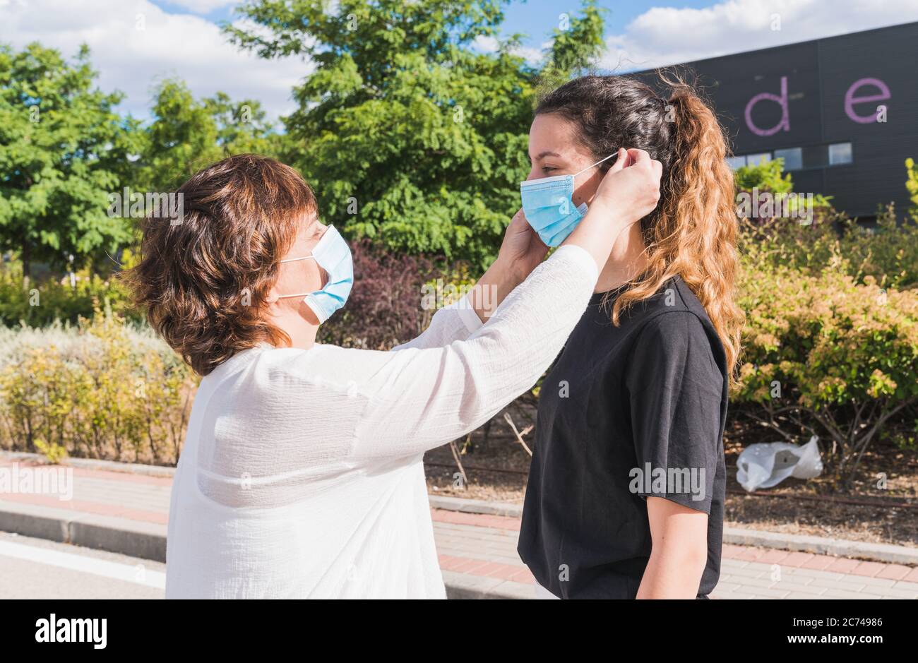 Nuovo normale. Madre e figlia che si proteggono contro il coronavirus. Madre mette sua figlia in una maschera per proteggerla dalla pandemia. Co Foto Stock