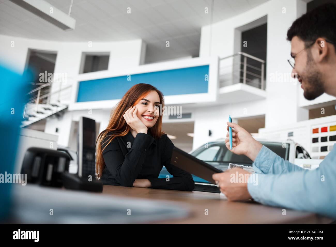 Il venditore della concessionaria di auto spiega i dettagli del contratto a una cliente femminile positiva Foto Stock