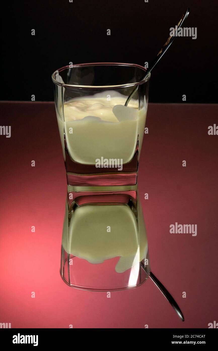 Yogurt greco in un vaso di vetro con cucchiaio su fondo rosso e nero primo piano. Foto Stock