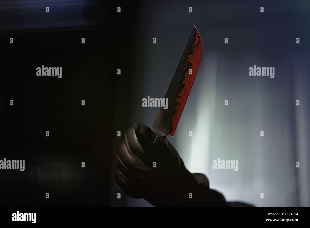 Un uomo con un coltello sanguinoso in piedi in appartamento, mani guanti in pelle, rapina armata, spietato assassino Foto Stock