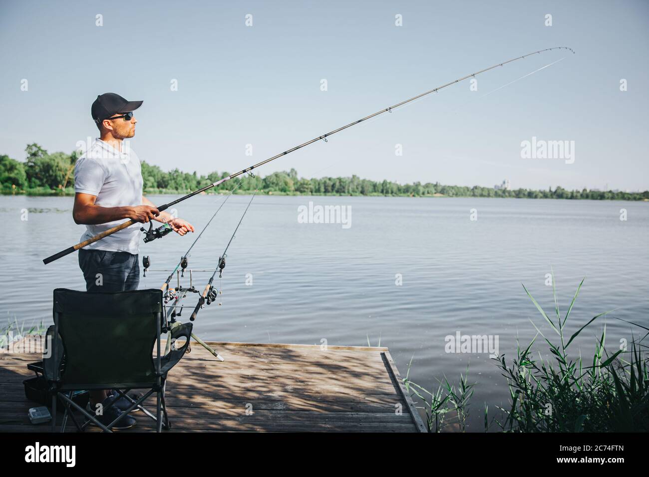 Pesca di pescatori giovani sul lago o sul fiume. Vista laterale del ragazzo adulto che si affaccia sul fiume o sul lago. Uomo che tiene l'asta nelle mani. Giornata soleggiata bella per ottenere fr Foto Stock