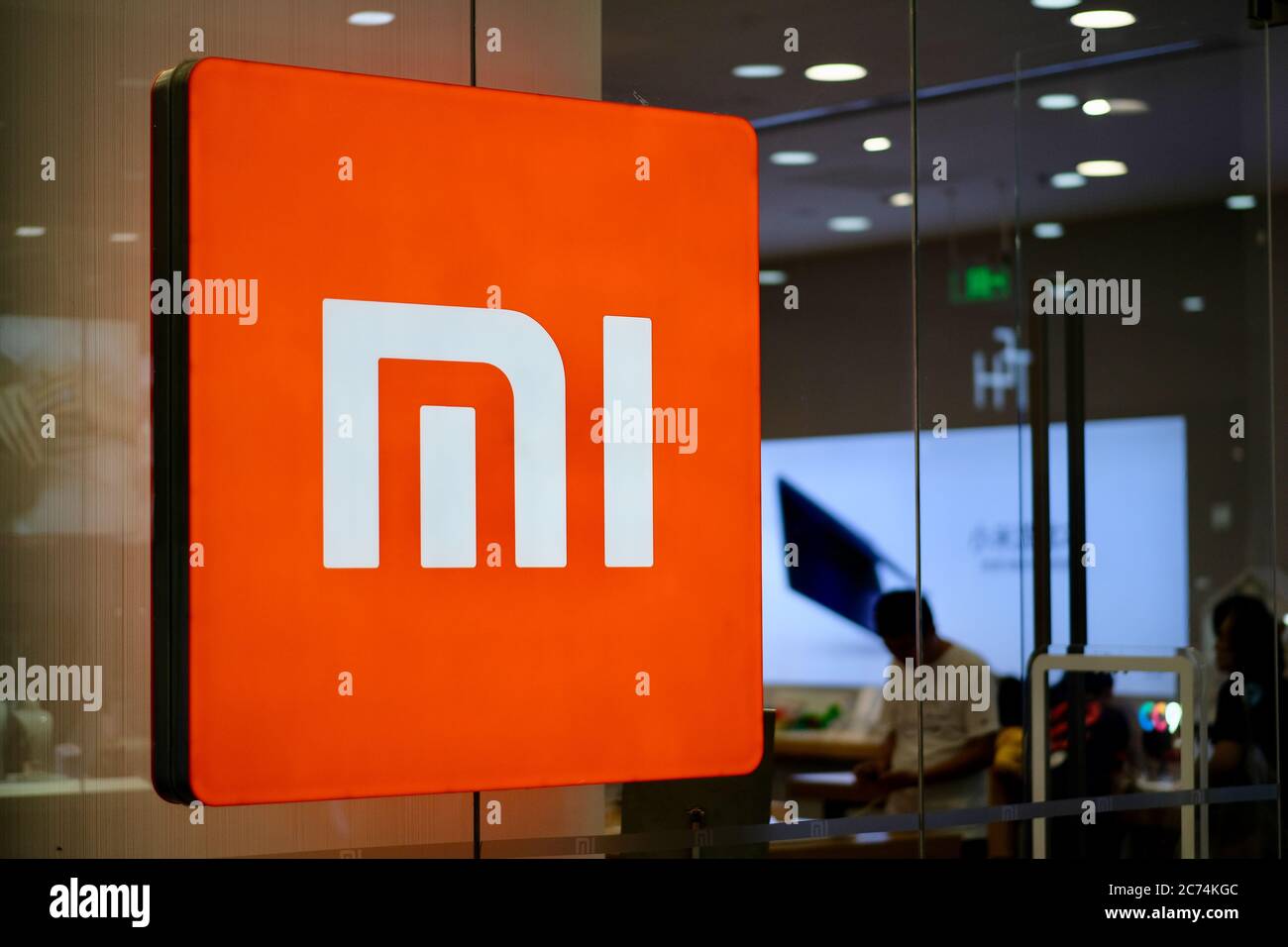 Primo piano il brillante logo di Xiaomi sulla scatola luminosa sulla parete di vetro del negozio. Un'azienda elettronica cinese Foto Stock