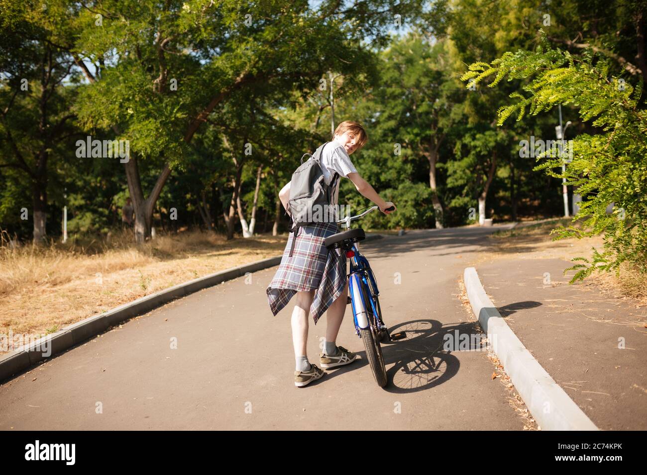 Giovane uomo con zaino che guarda con la macchina fotografica mentre si va in bicicletta nel parco. Ragazzo fresco che passa il tempo nel parco con la bicicletta Foto Stock