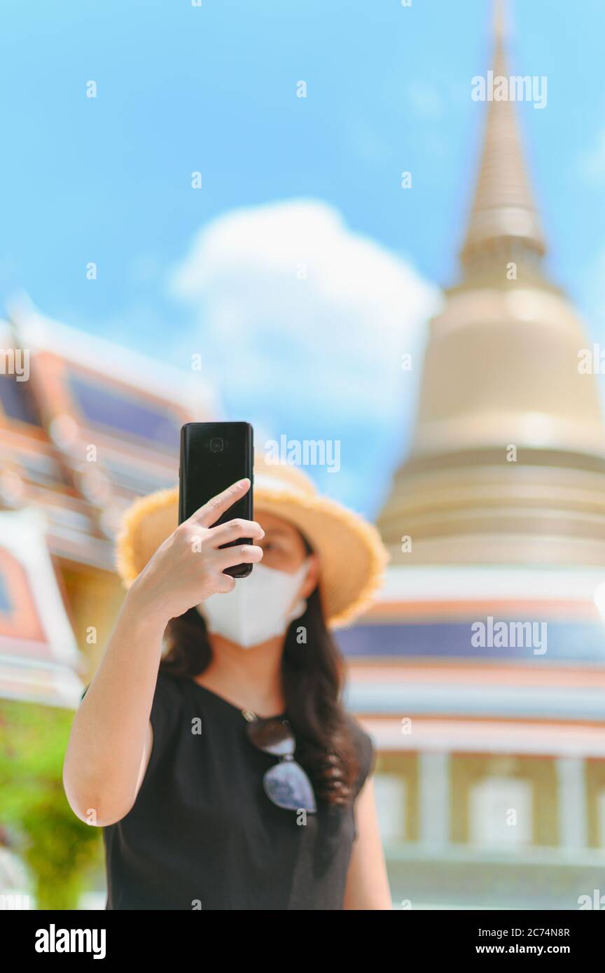 Donna asiatica con maschera godere felice prendere un selfie foto in wat thai. Nuovo stile di vita normale di viaggio dopo il concetto di virus covid. Foto Stock