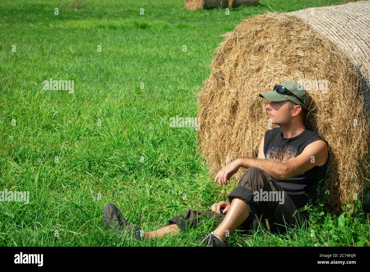 Seduto uomo al prato verde, basato su una balla di fieno, estate soleggiato giorno Foto Stock