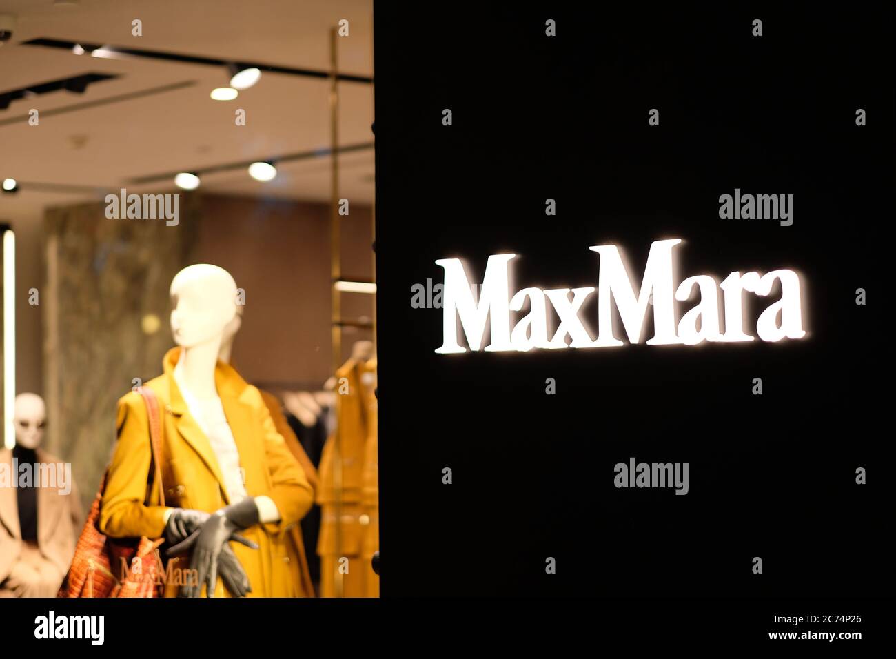 Primo piano luminoso logo MaxMara lucido sulla parete esterna nera del negozio. Offuscare i vestiti all'interno come sfondo. Un marchio di moda italiano Foto Stock
