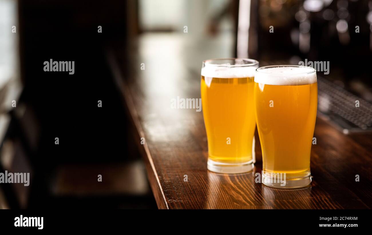 Ritrovo con gli amici in un pub e in un set di birre. Due bicchieri di birra leggera con schiuma sul bancone del bar in legno nella luce del giorno all'interno del pub Foto Stock