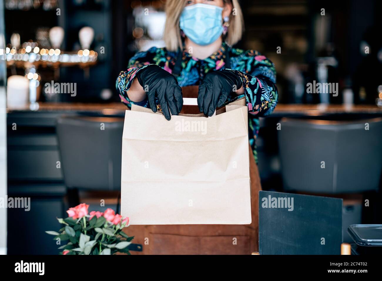 donna alla porta del ristorante che dà cibo pronto in una borsa di carta con - take away in tempo di scoppio del coronavirus Foto Stock