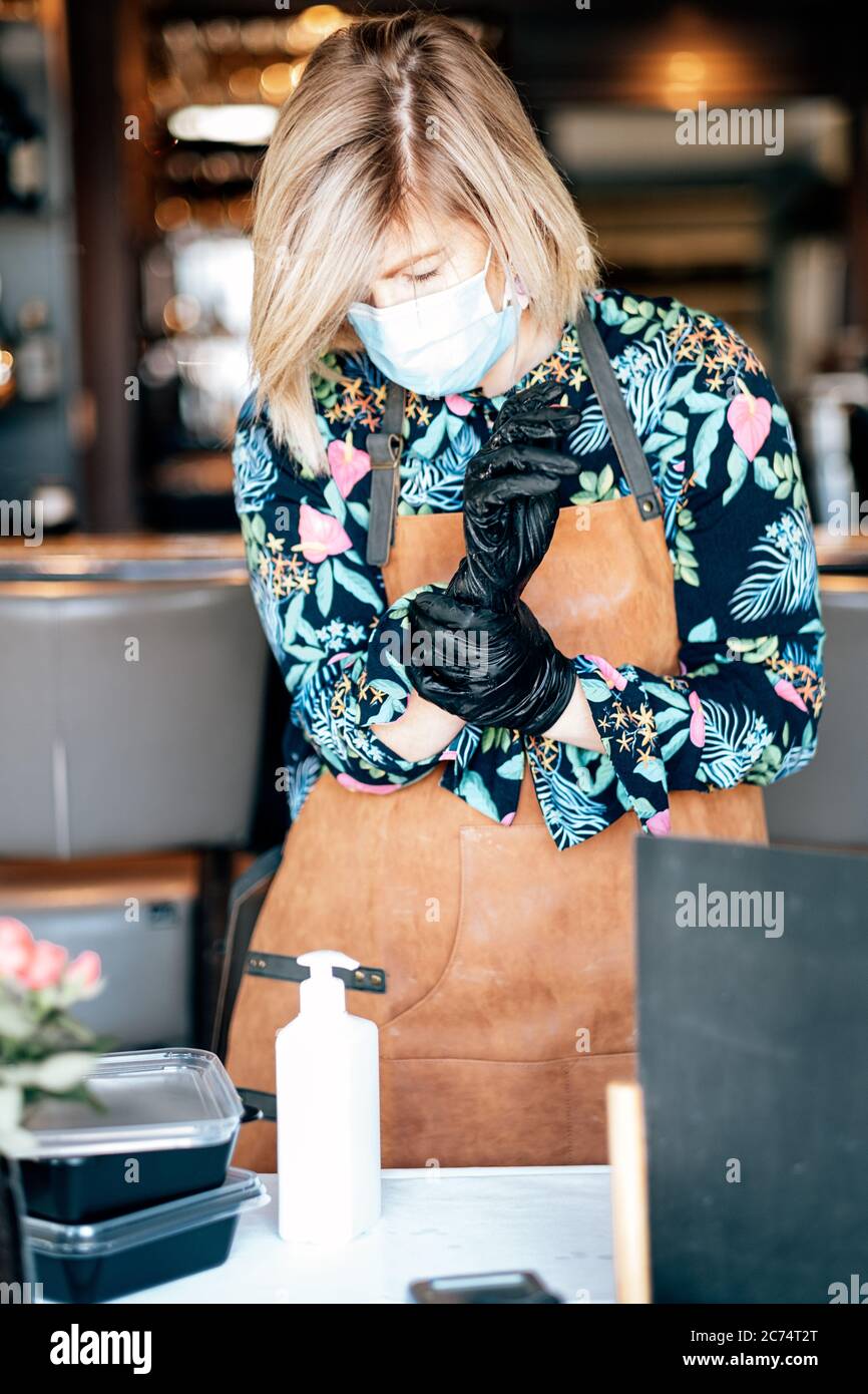 il lavoratore del ristorante di takeaway del cibo si prepara a lavorare con i guanti, la maschera e il gel antisettico - protezioni di base nel tempo di scoppio del coronavirus Foto Stock