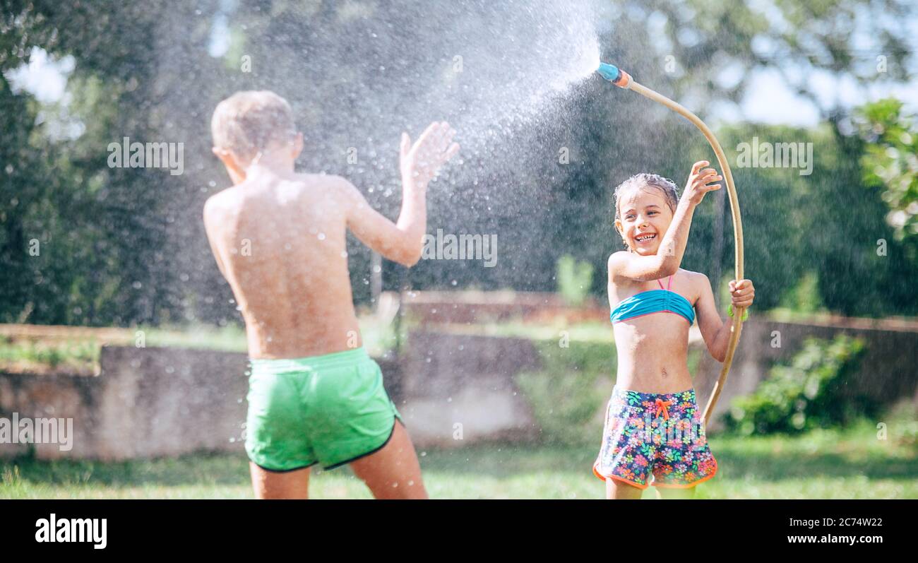 Due bambini, fratello e sorella, si divertono, quando si gioca con il tubo di irrigazione nel giardino estivo Foto Stock