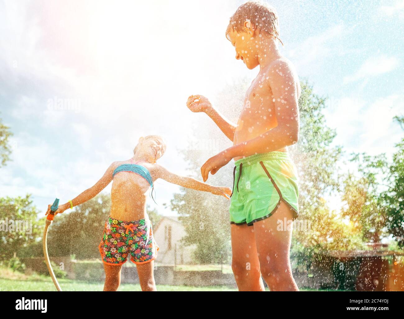 Fratello e sorella si divertono, quando si gioca con annaffiatura tubo in giardino estivo Foto Stock