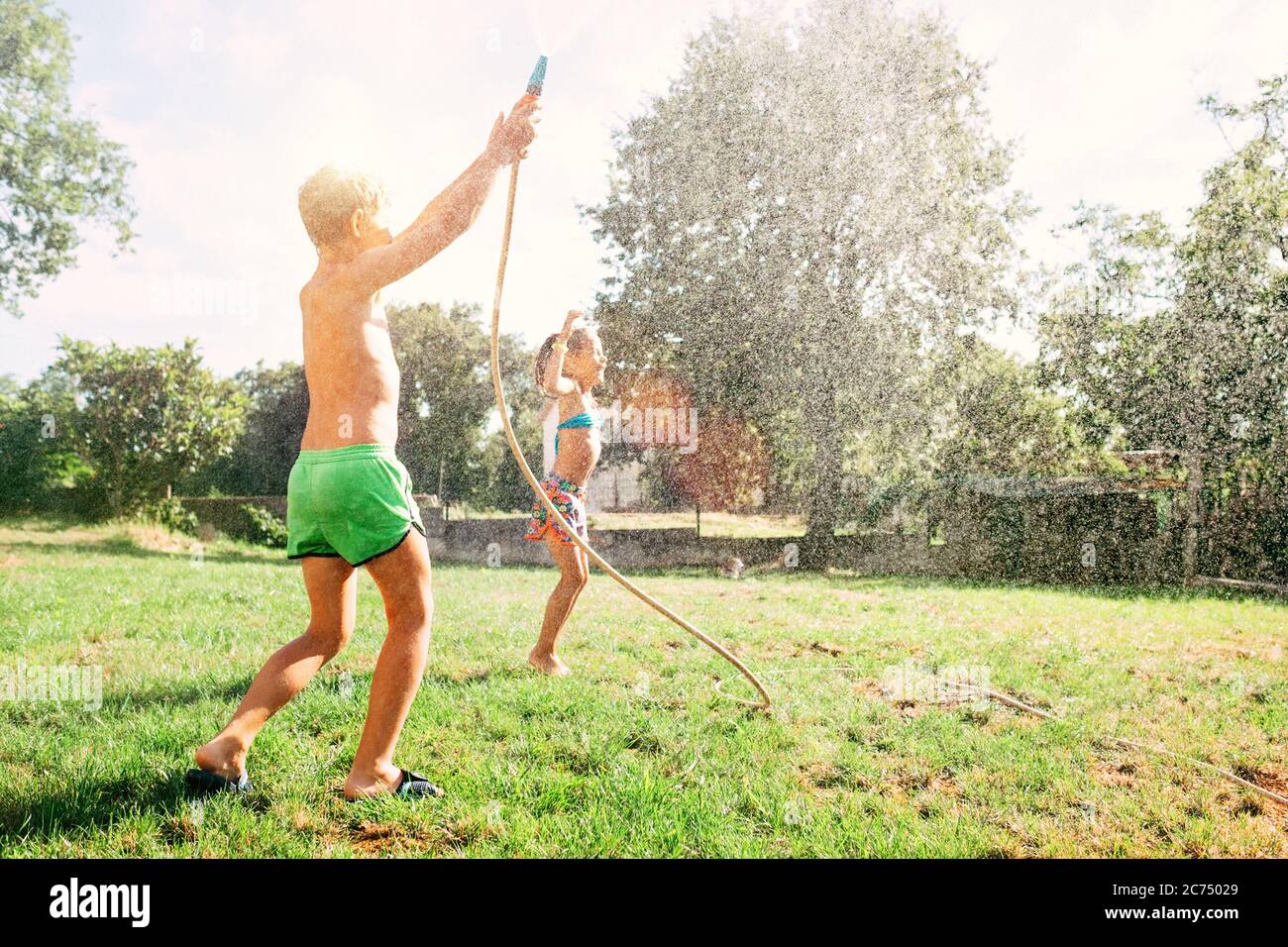 Due bambini giocano insieme in giardino, caldo giorno d'estate, fanno un raim da giardino annaffiatura tubo Foto Stock