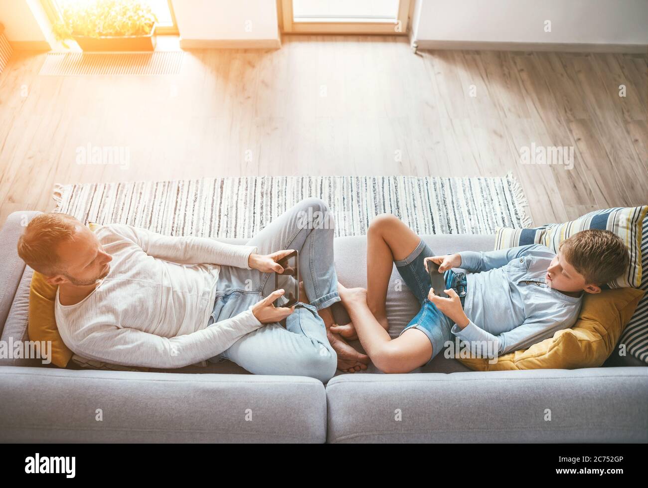 Padre e figlio Losted in dispositivi elettronici. Giocano con tablet e gamepad seduti in salotto Foto Stock