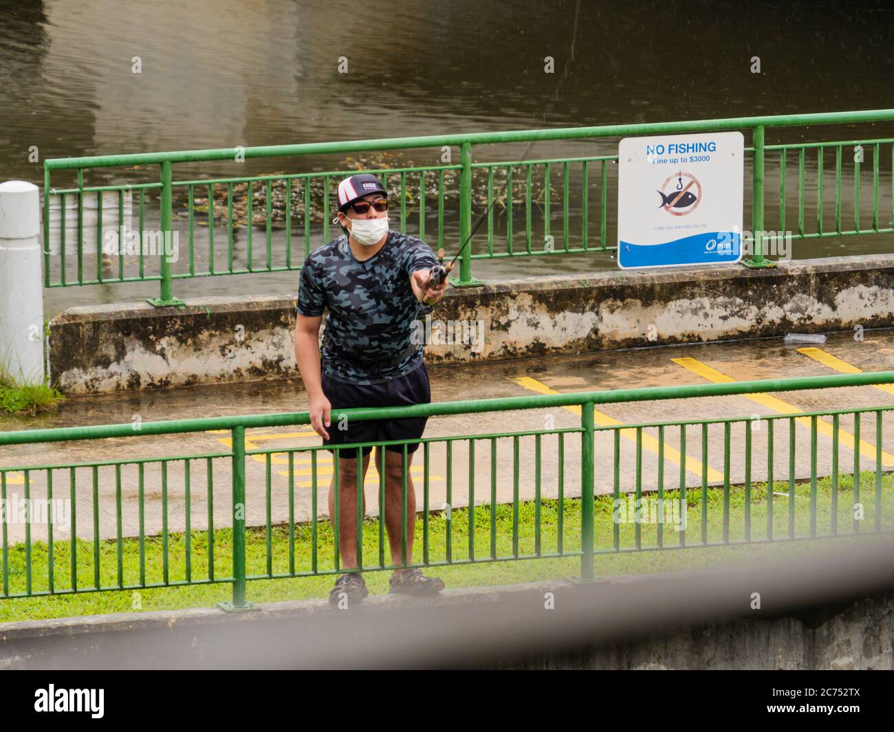 SINGAPORE – LUGLIO 09 2020 – l'uomo in una maschera protettiva che infrangerà la legge pescando illegalmente accanto a un cartello di non pesca presso il sentiero del connettore del parco a SPR Foto Stock