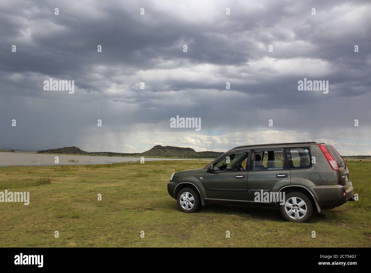 Un'auto in paesaggio africano - Rustfontein Dam in Sud Africa, sotto forti nuvole di pioggia Foto Stock