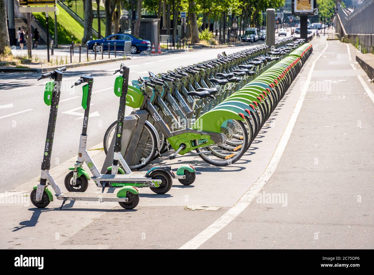 Una flotta di circa sessanta biciclette condivise Velib, insieme a tre scooter elettrici Lime, sono allineati ordinatamente in una stazione di attracco a Parigi, Francia. Foto Stock
