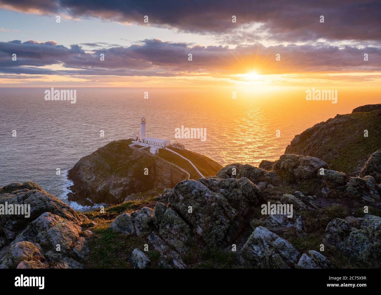 Il sole di setting highlights Sud pila faro sull isola di Holyhead, Galles, visto dalla rupe su una serata blustery in primavera. Foto Stock