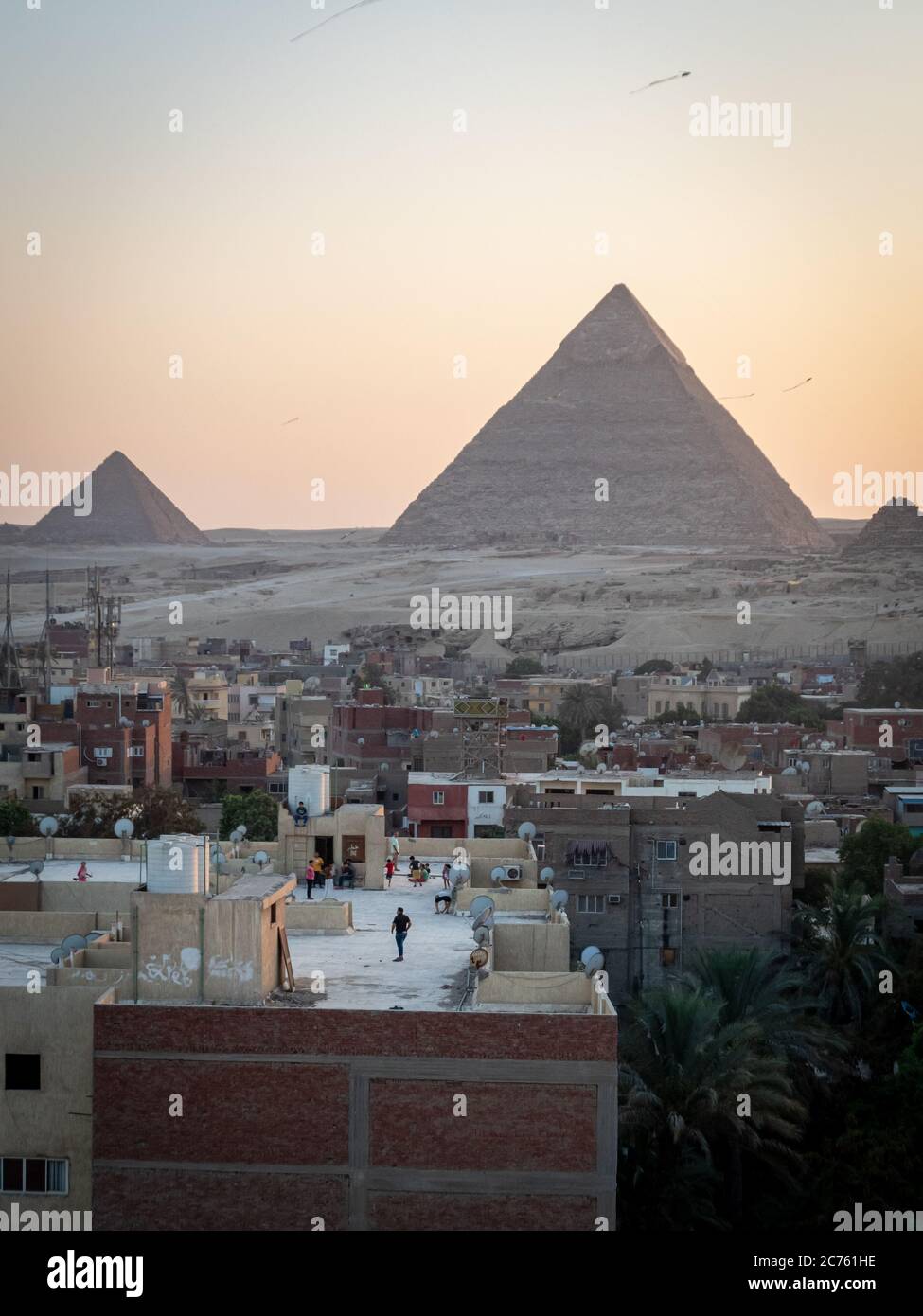 Vista delle piramidi al tramonto dal tetto di giza e bambini che giocano con aquiloni Foto Stock