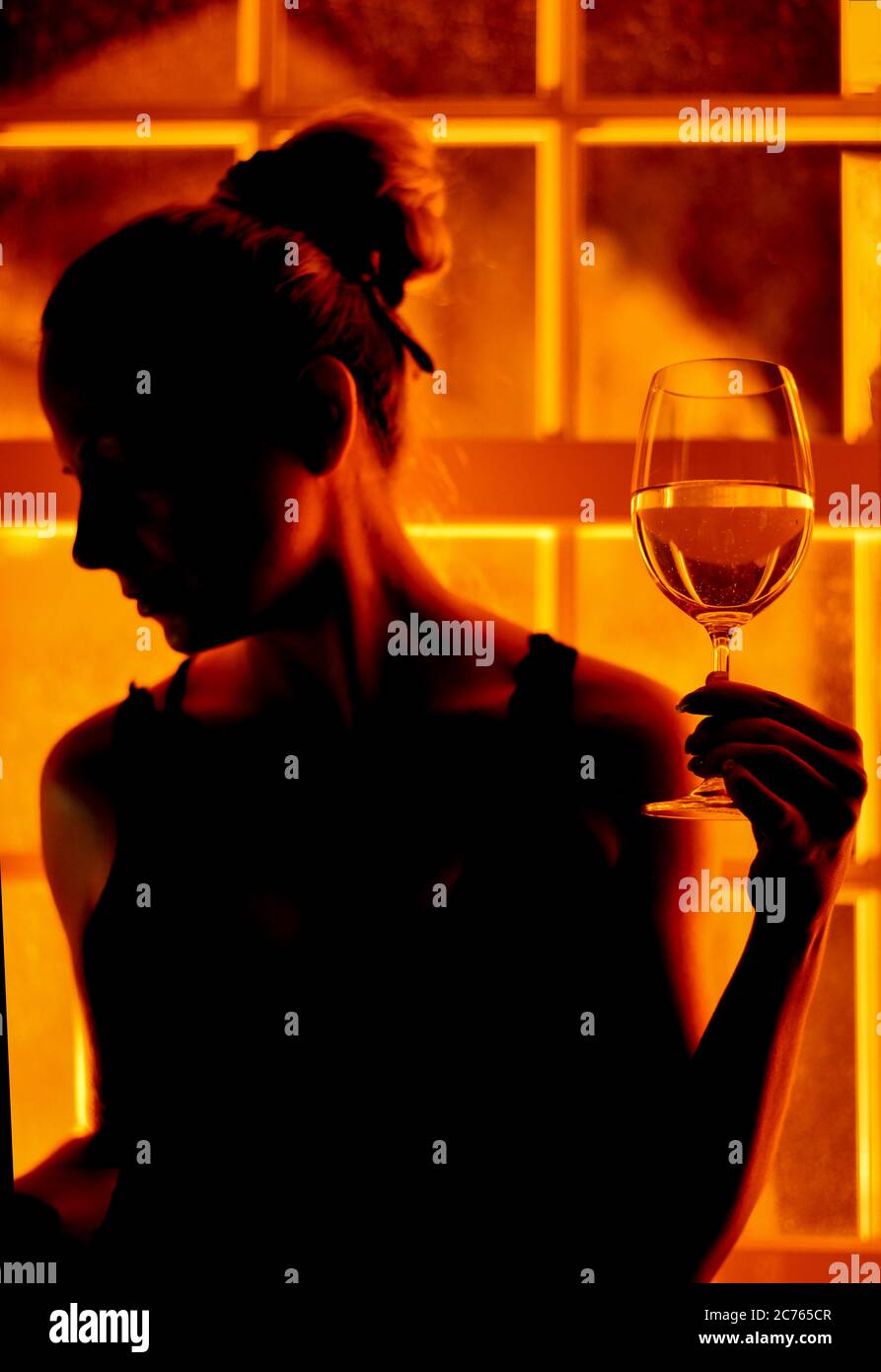 Donna che tiene un bicchiere di vino vicino alla finestra di notte a casa Foto Stock
