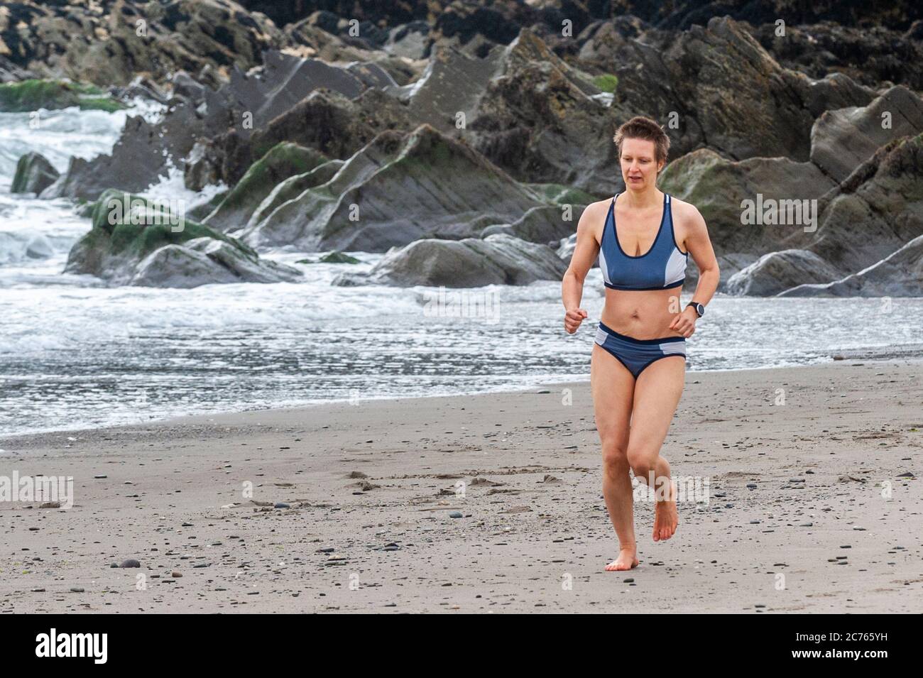 Owenahincha, West Cork, Irlanda. 14 luglio 2020. Una donna corre sulla spiaggia di Red Strand, West Cork, nonostante il freddo. Credit: Notizie dal vivo di AG/Alamy Foto Stock