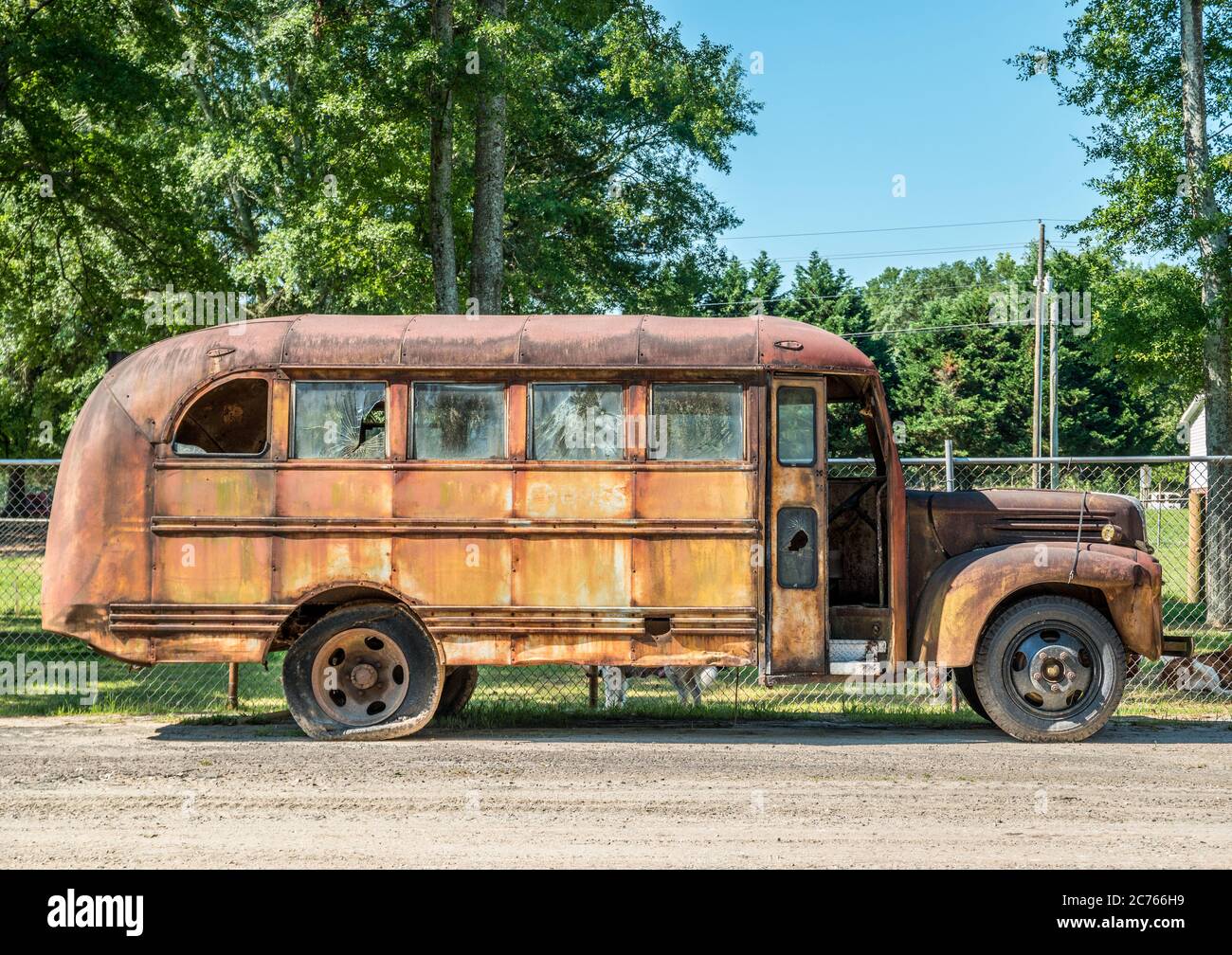 Un vecchio autobus scolastico arrugginito con finestre in vetro rotte e pneumatici piatti si trova trascurato vista laterale all'aperto Foto Stock