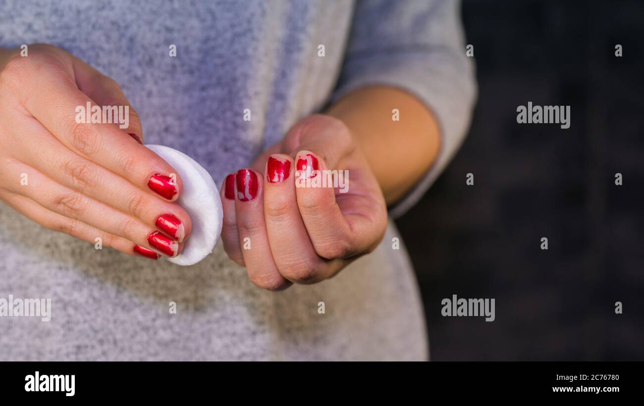 Donna rimuove lo smalto per unghie. Donna smalto rosso per unghie con tampone in cotone bianco. Foto Stock