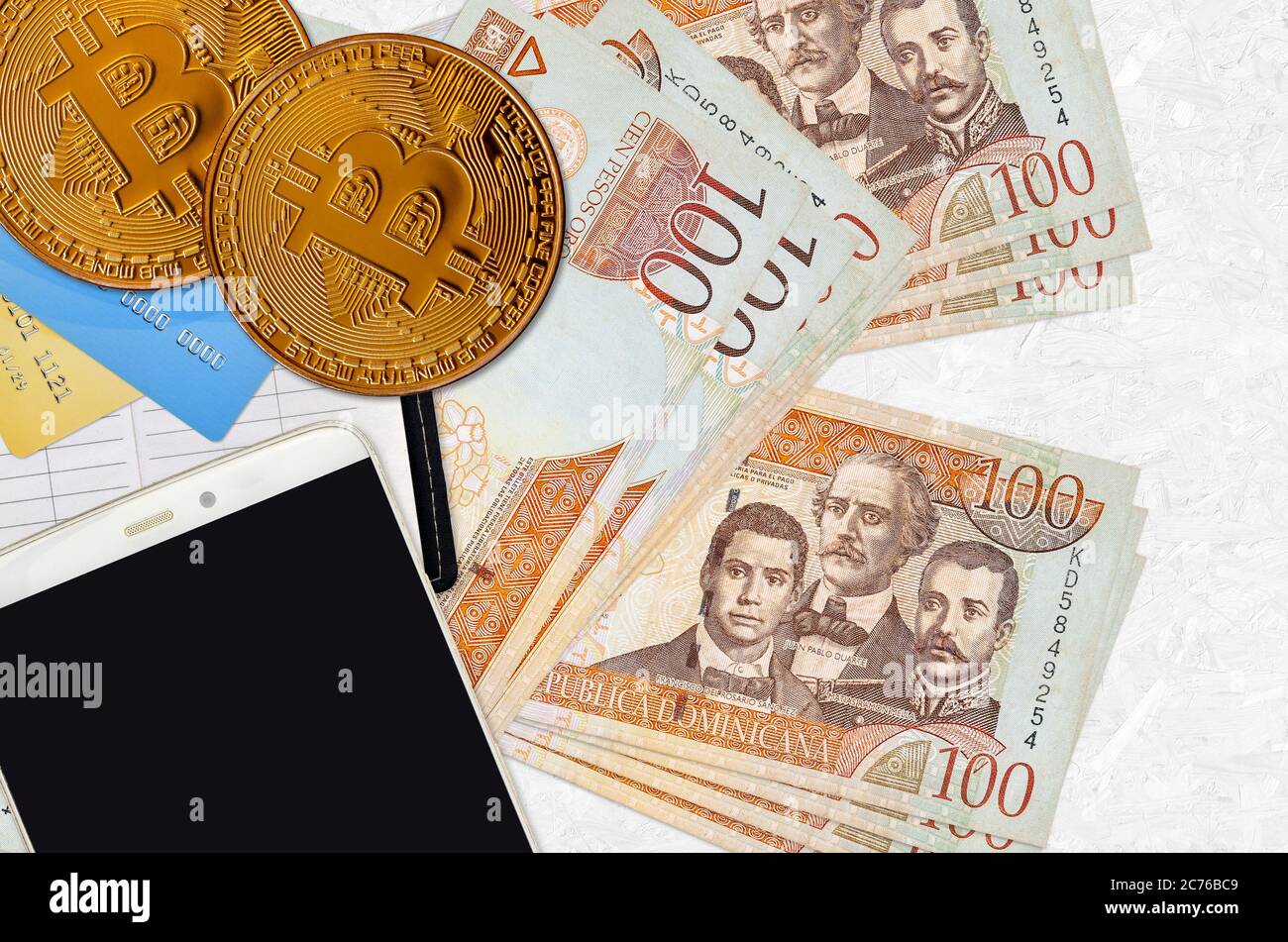100 pesos dominicani e monete d'oro con smartphone e carte di credito. Concetto di investimento in criptovaluta. Crypto mining o transazione commerciale Foto Stock