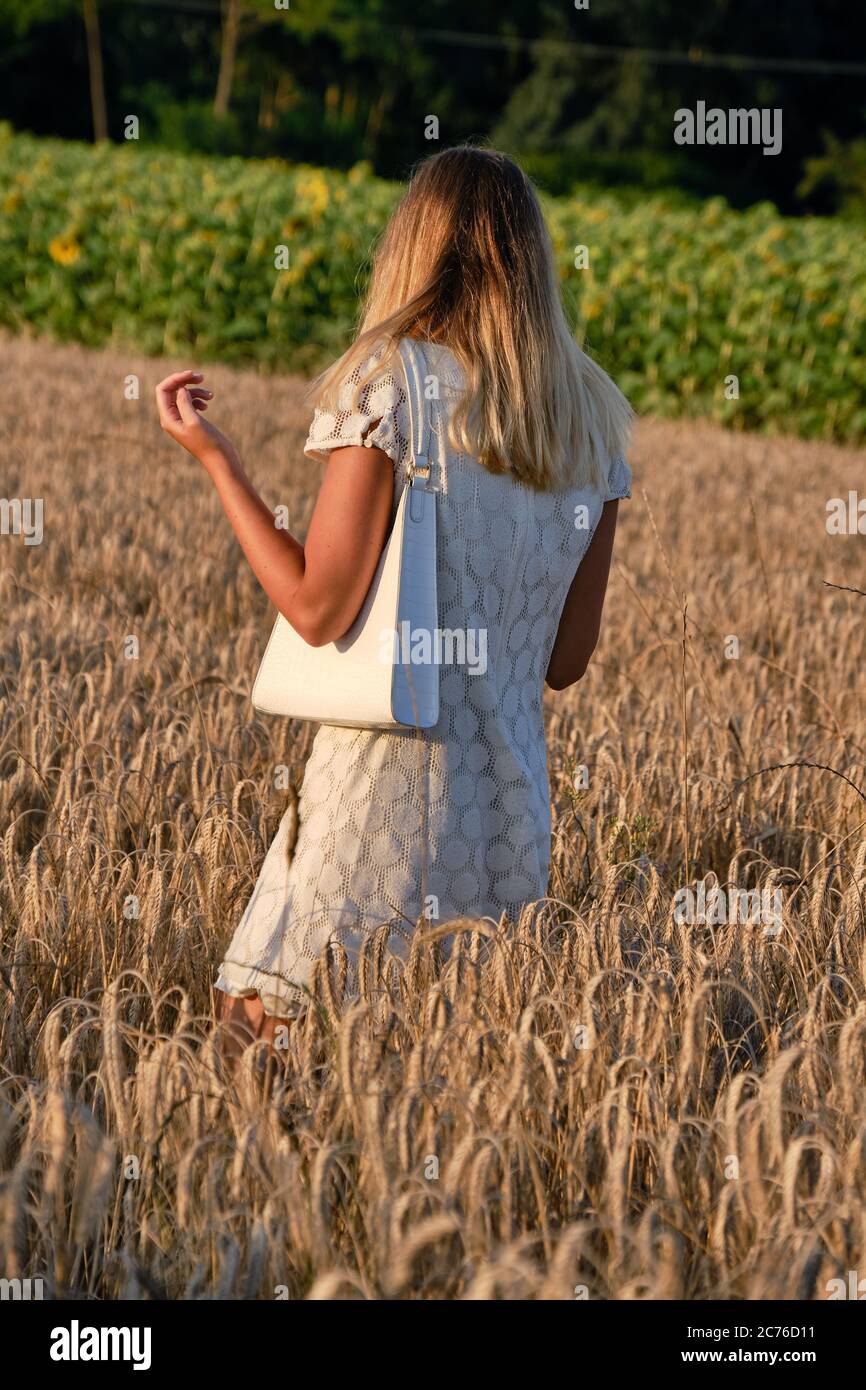 Foto a lunghezza intera di giovane donna attraente in campo con il sole che splende in background. Modello femminile di moda all'aperto con abito bianco in campagna Foto Stock