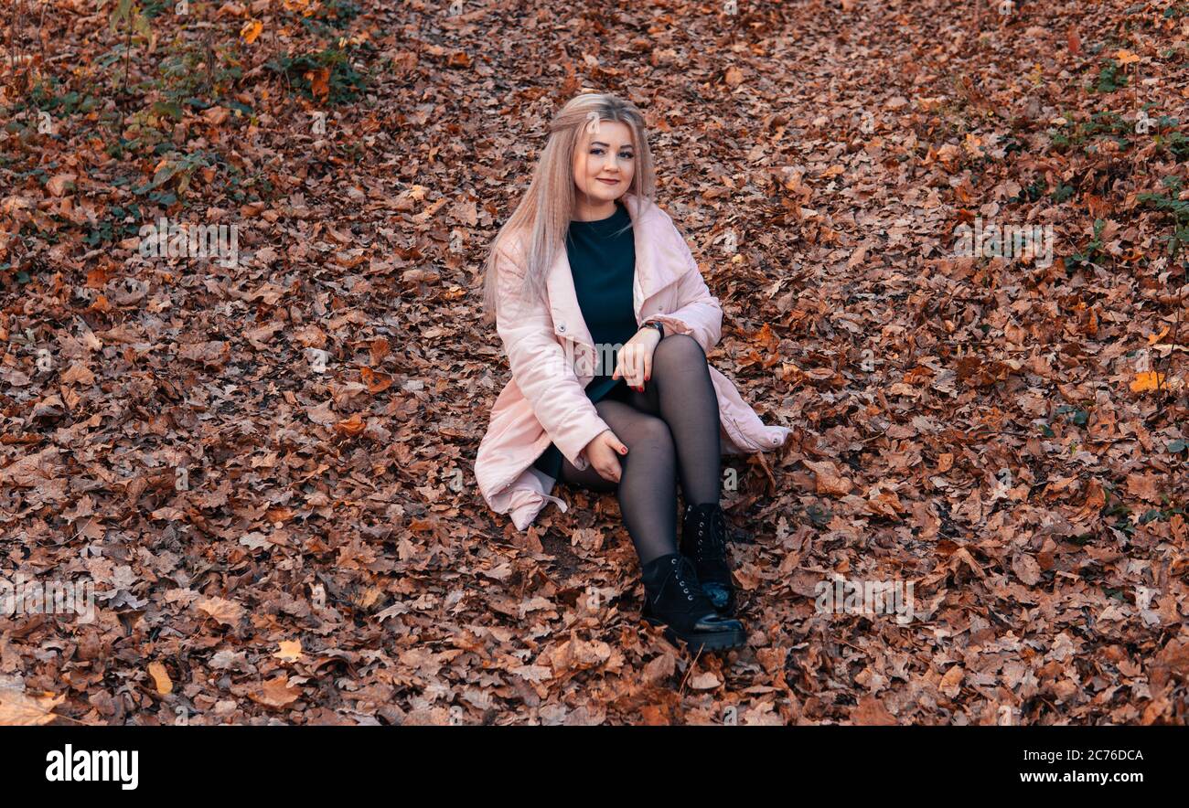 Una giovane donna piacevole in abiti casual con capelli lunghi è seduta nella foresta di autunno. Foto Stock