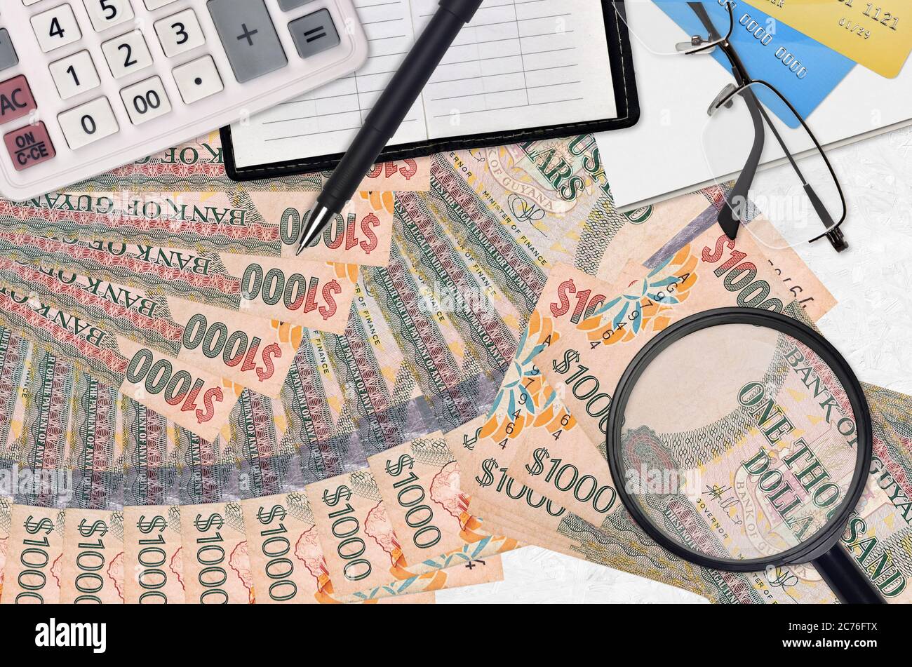 1000 dollari guyanesi bollette e calcolatrice con occhiali e penna. Concetto di stagione di pagamento fiscale o soluzioni di investimento. Ricerca di un lavoro con un alto stipendio Foto Stock