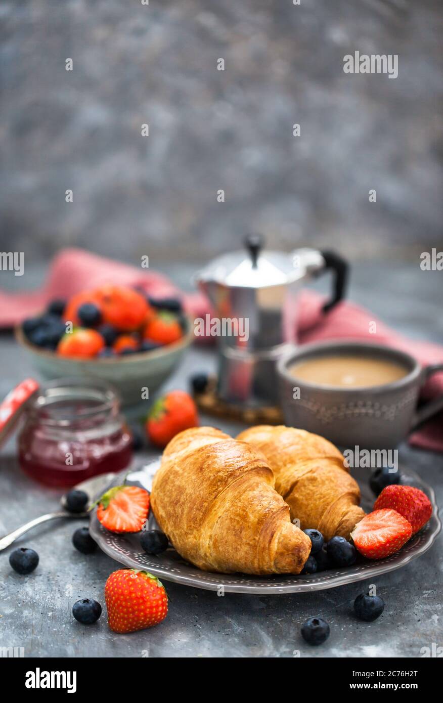 Colazione continentale con croissant, frutti di bosco freschi, caffè e marmellata, sfondo grigio Foto Stock