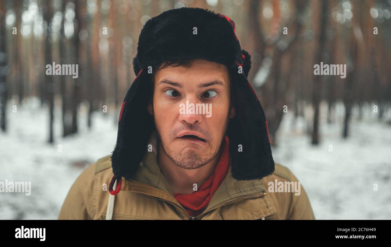 Uomo grimaces in foresta nella stagione invernale. Ritratto di pazzo maschio che indossa copricapo e grimacing faccia da vicino nella foresta invernale. Foto Stock