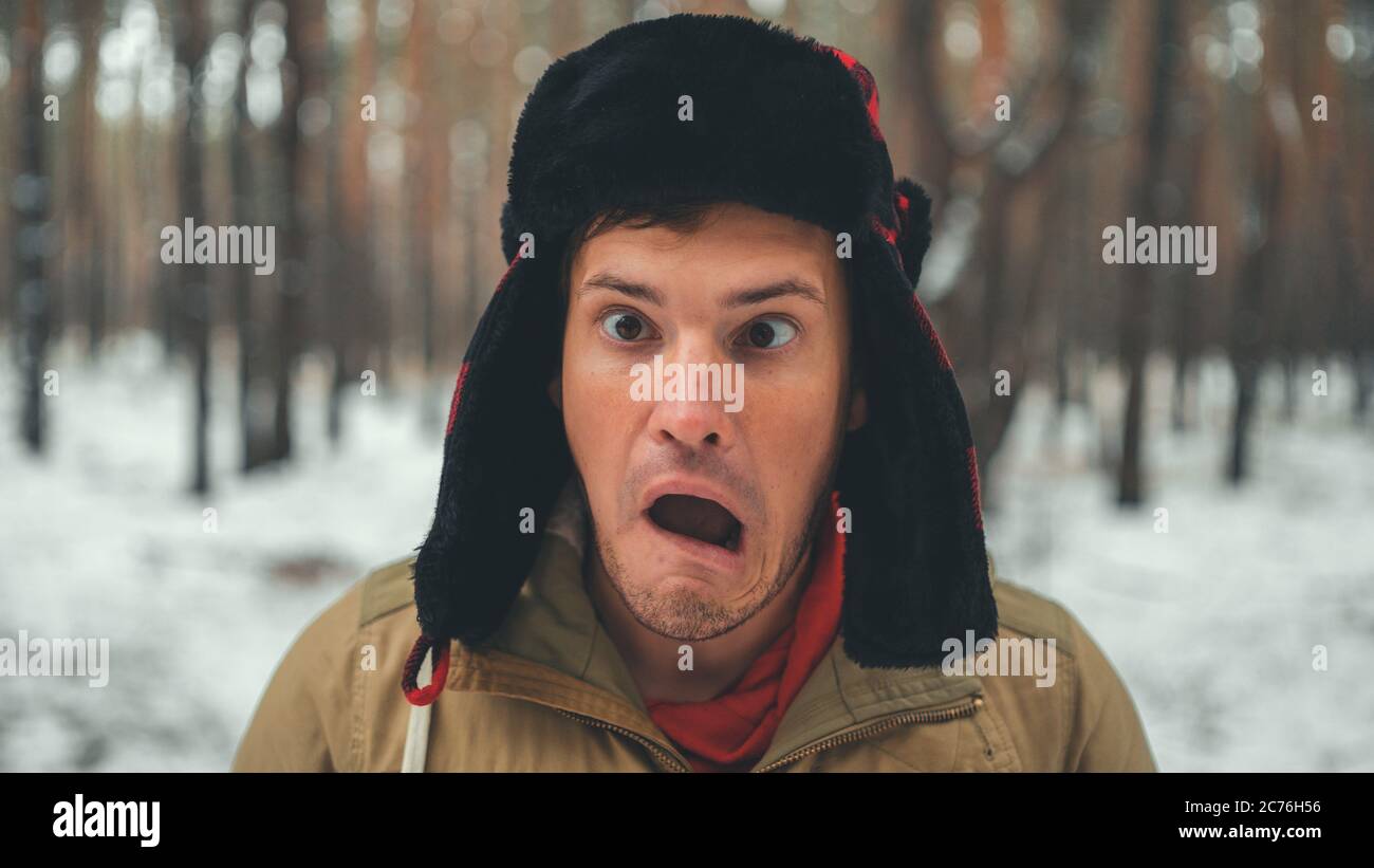 Uomo grimaces in foresta nella stagione invernale. Ritratto di pazzo maschio che indossa copricapo e grimacing faccia da vicino nella foresta invernale. Foto Stock