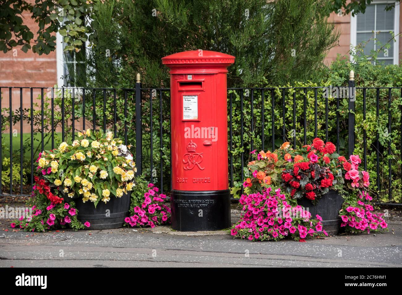 Fiori e piante intorno a un iconico box postale rosso su Main Street nel villaggio di Bothwell, Lanarkshire. Foto Stock