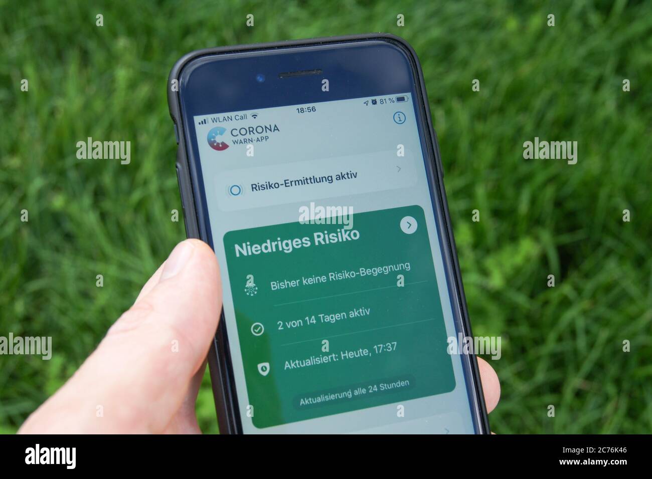 Corona avvisa l'app del governo federale tedesco su uno smartphone tenuto in una mano di un uomo davanti a sfondo erba. Viene visualizzato il messaggio "basso rischio". Foto Stock