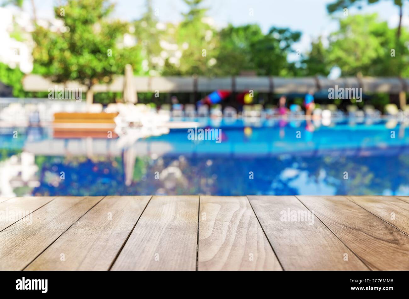 Tavolo in legno su sfondo piscina sfocato con sedie da spiaggia Foto Stock