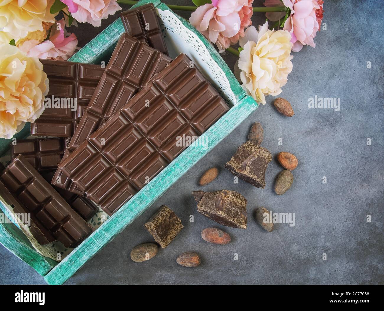 Barrette di cioccolato in una scatola vintage. Chicchi di cioccolato, fiori, pezzi di cioccolato sparsi su uno sfondo textural Foto Stock