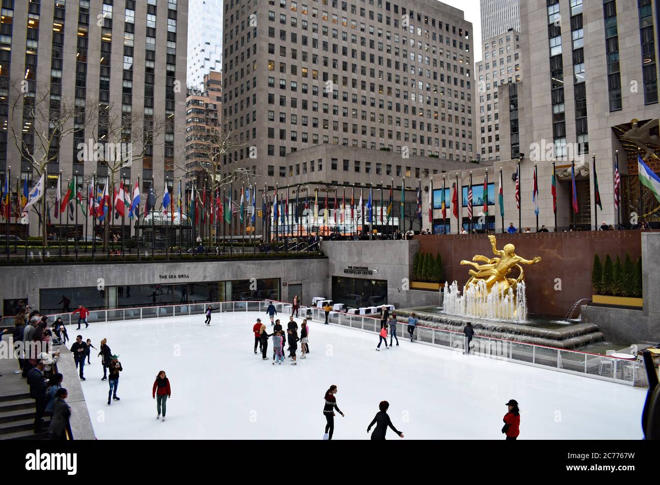Persone che pattinano sulla pista di pattinaggio nel Rockefeller Center. La statua dorata del Prometheus è vista così come le bandiere che costeggiano la parte superiore intorno alla pista. Foto Stock