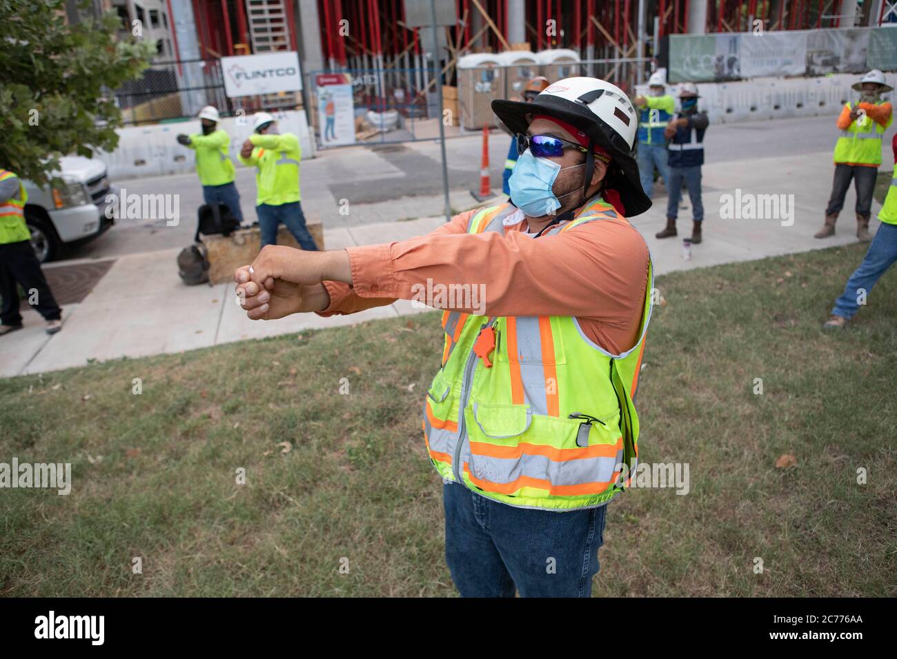 Austin, TX USA 14 luglio 2020: I lavoratori edili che indossano rivestimenti di faccia partecipano a stretching e un programma di esercizio breve come si preparano per un turno di otto ore nel calore di 105 gradi del Texas. Gli equipaggi sono al secondo piano di un edificio a 53 piani, mentre prendono precauzioni contro la pandemia del coronavirus. Foto Stock