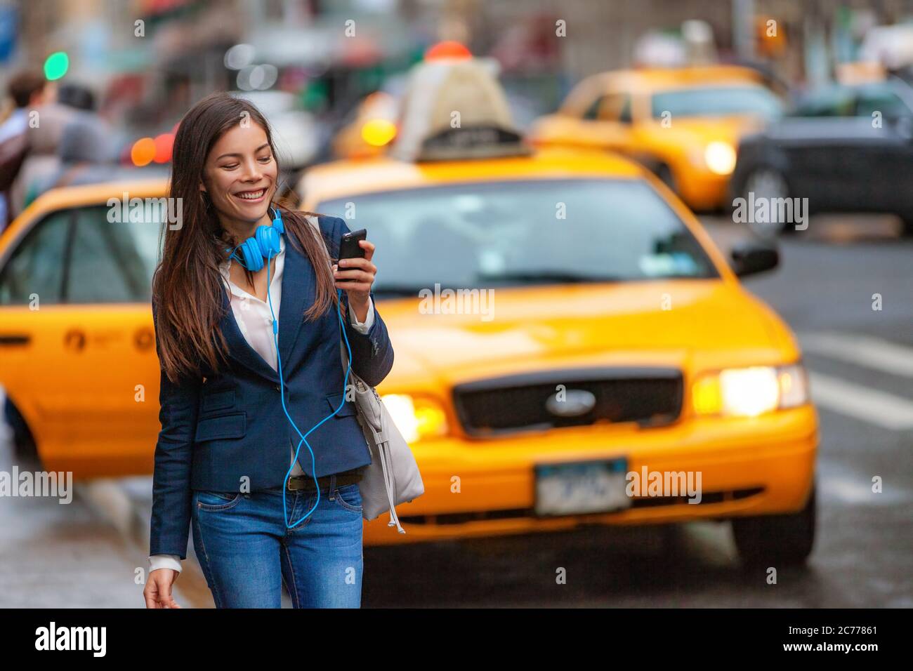 Giovane donna che cammina a New York usando l'app per il telefono per un giro in taxi con le cuffie che si trasferiscono dal lavoro. Ragazza asiatica felice di inviare SMS su smartphone Foto Stock