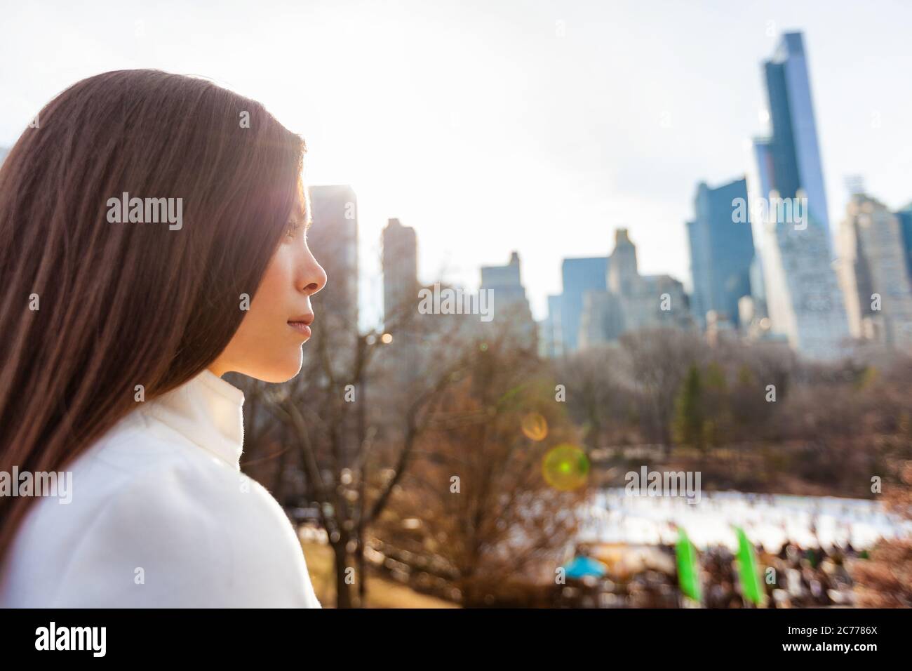 Donna asiatica di New York City che cammina in inverno a Central Park vicino alla pista di pattinaggio che guarda lo sfondo dello skyline di New York. Vita urbana Foto Stock