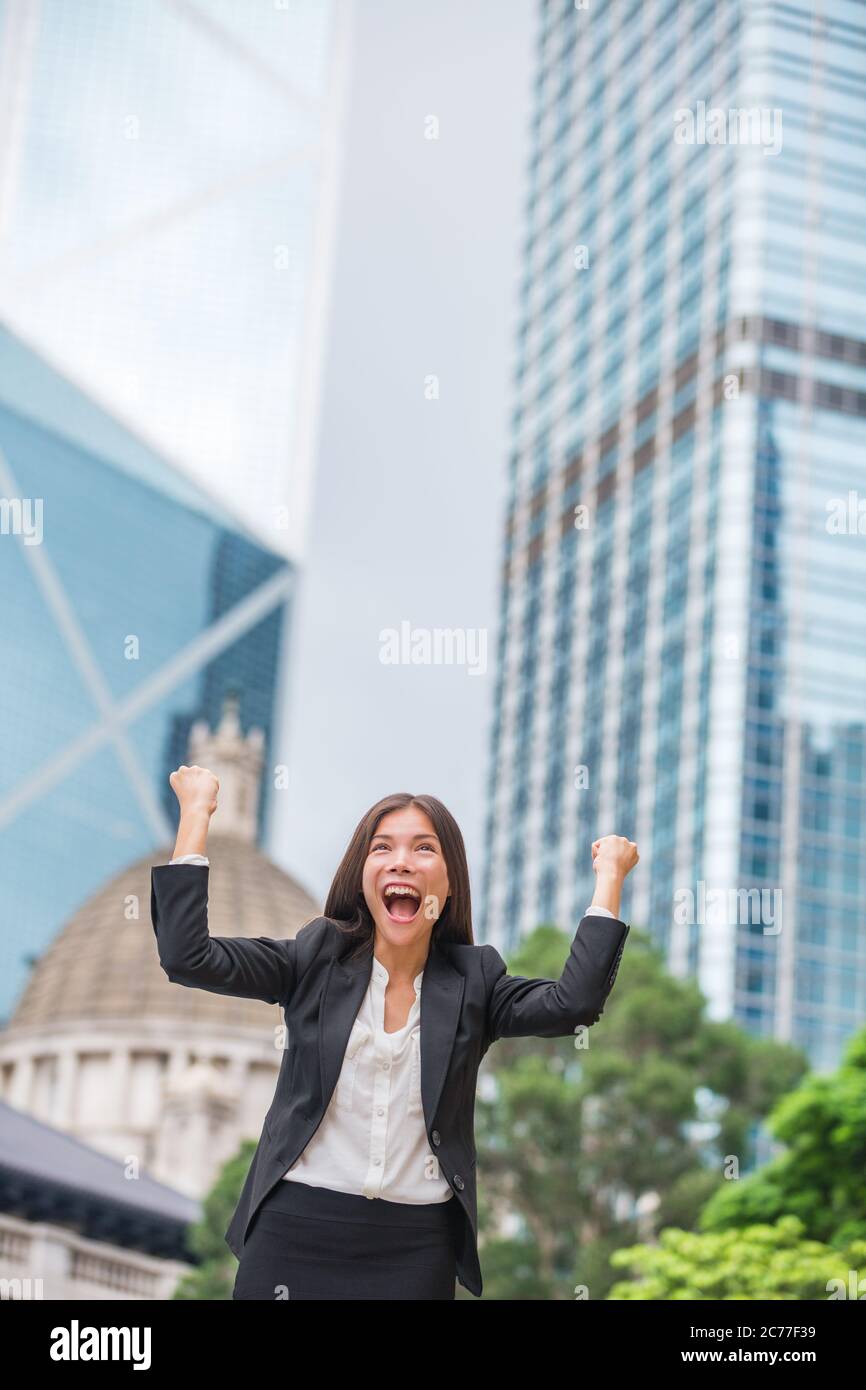 Donna di affari successo felice a Hong Kong che celebra il commercio riuscito con le armi in su le mani sollevate nell'aria che vince. Cinese multirazziale giovane Foto Stock