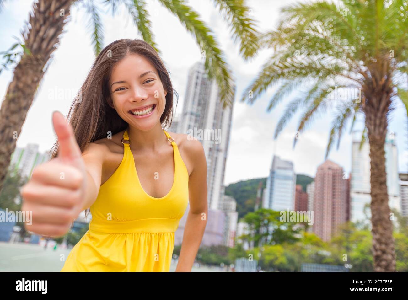 Ragazza cinese felice facendo pollici in su nella soddisfazione nella città di Hong Kong, Asia stile di vita di viaggio della Cina. Giovane donna multirazziale sorridente Foto Stock