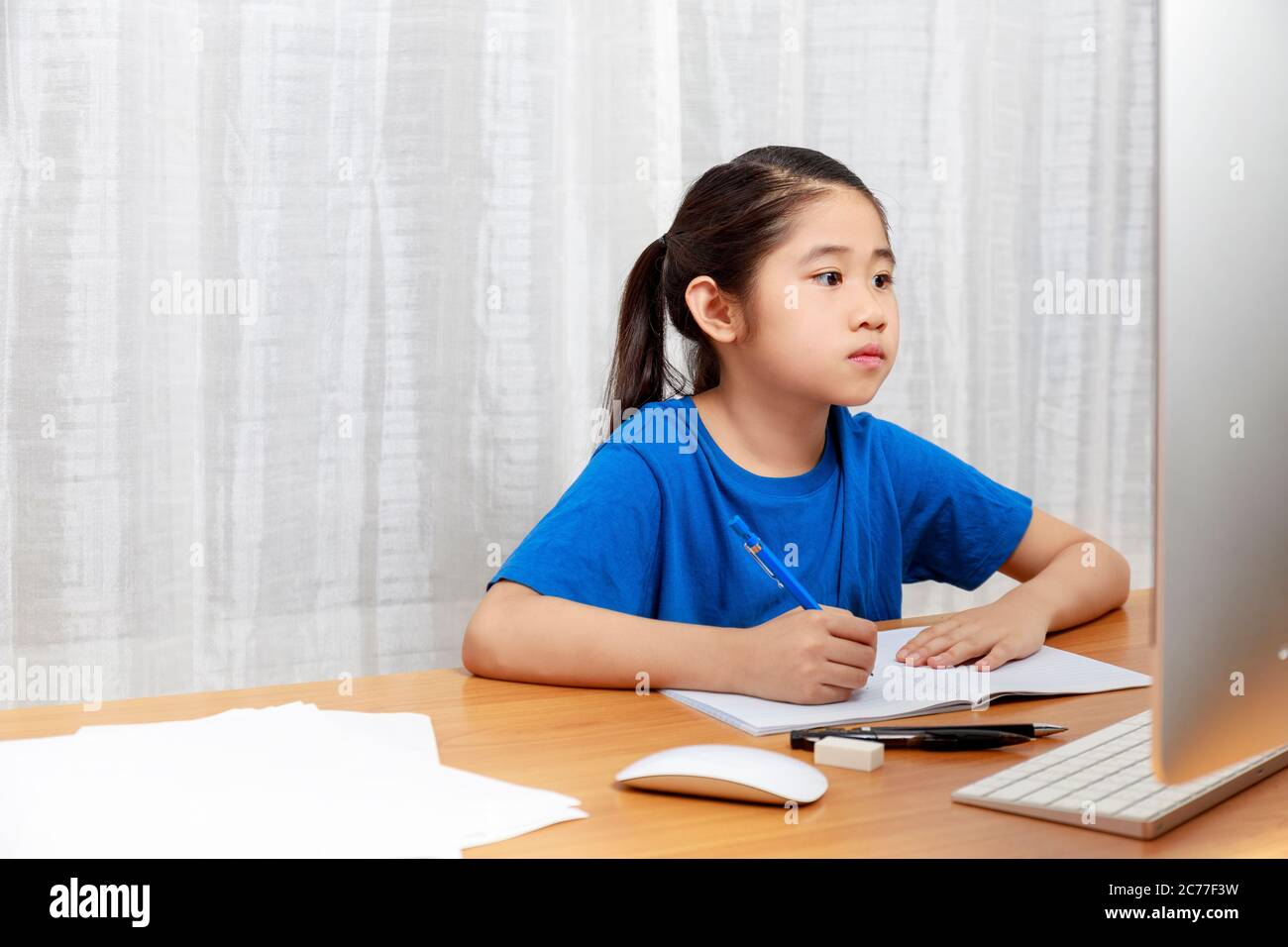 La bambina asiatica sta studiando in linea via il Internet che siede e scrive nel soggiorno a casa. Asia bambini che scrivono con matita su notebook. Su Foto Stock