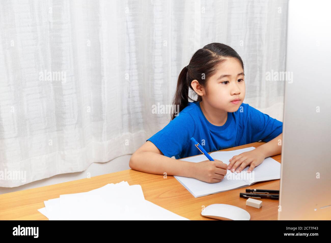 La bambina asiatica sta studiando in linea via il Internet che siede e scrive nel soggiorno a casa. Asia bambini che scrivono con matita su notebook. Onl Foto Stock