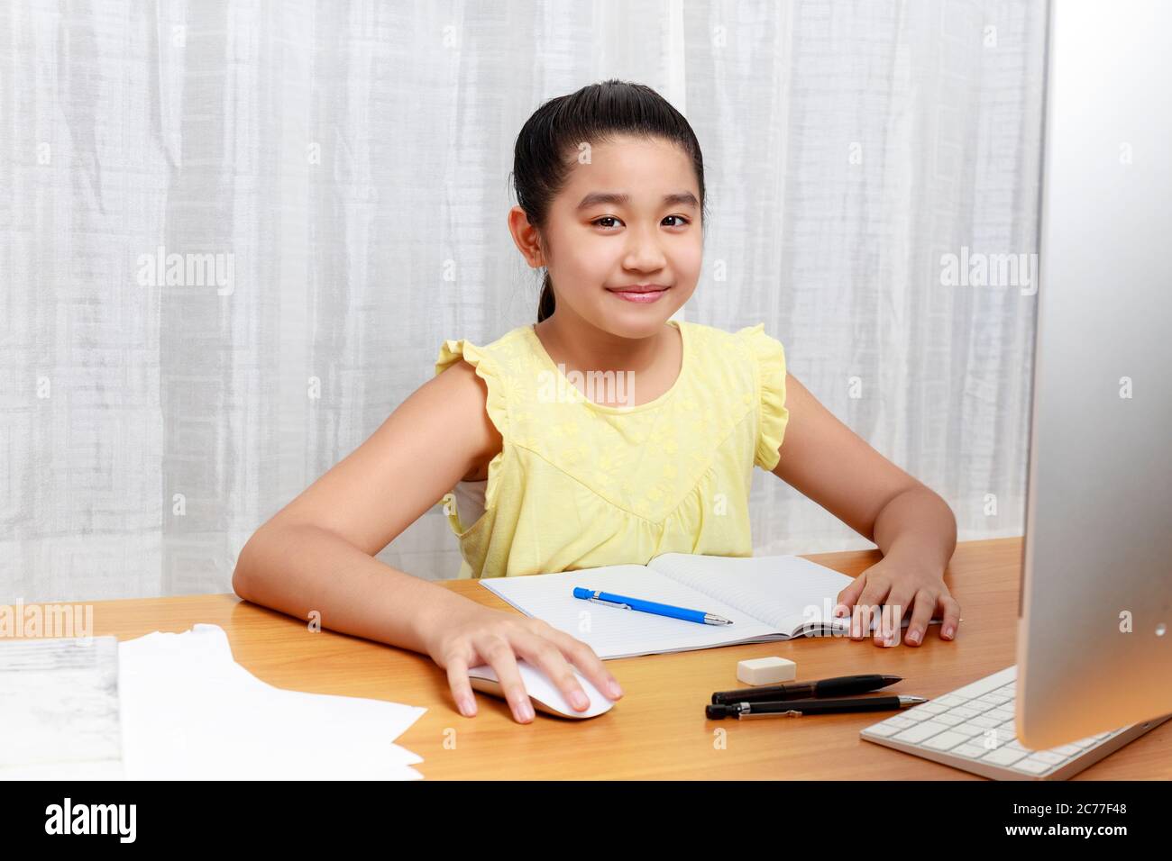 La bambina asiatica sta studiando in linea via il Internet che siede e scrive nel soggiorno a casa. Asia bambini che scrivono con matita su notebook. Onl Foto Stock