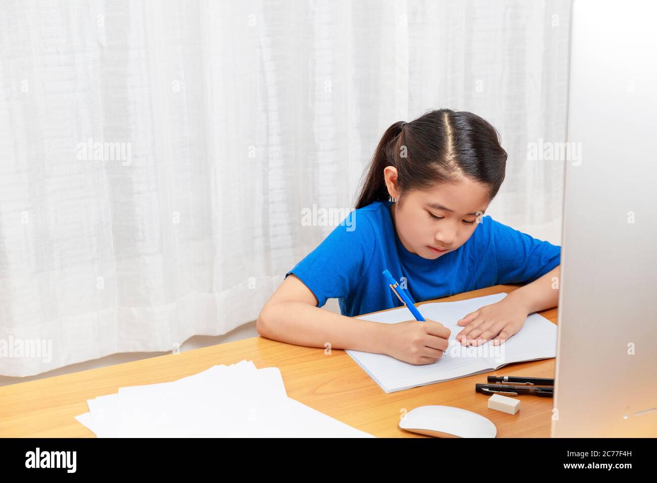 La bambina asiatica sta studiando in linea via il Internet che siede e scrive nel soggiorno a casa. Asia bambini che scrivono con matita su notebook. Su Foto Stock