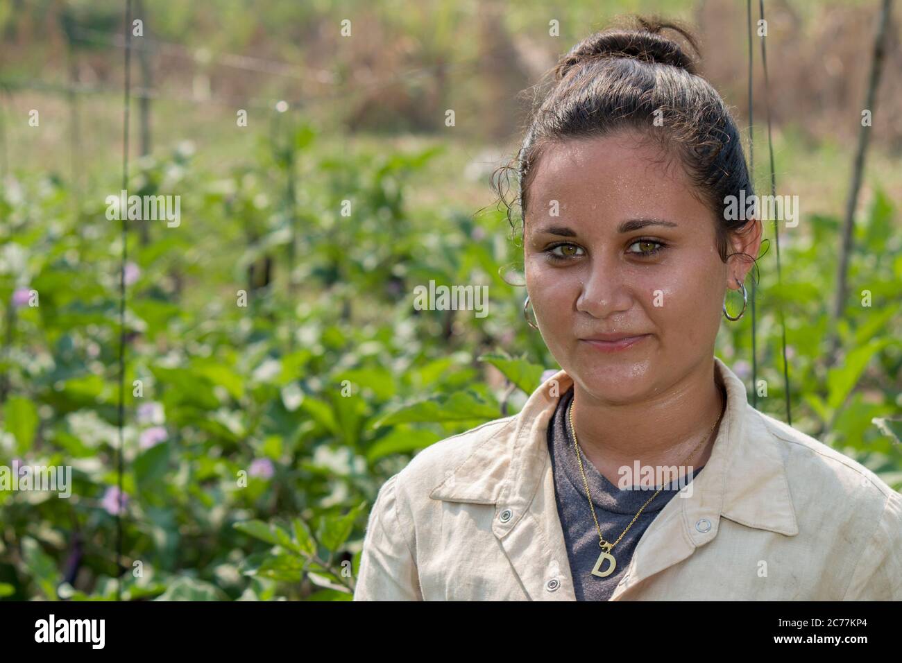 Giovane ragazza con occhi verdi che lavora duro in una fattoria di verdure sotto un sole forte nei tropici Foto Stock